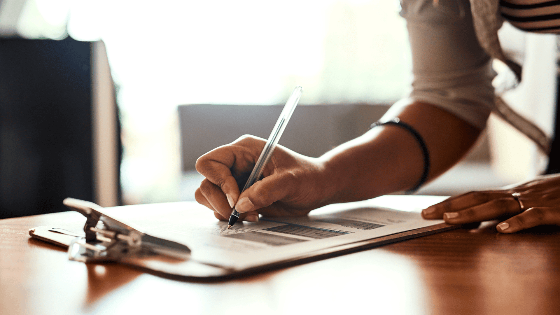 Close-up of a person signing a real estate disclosure form on a clipboard at a wooden table
