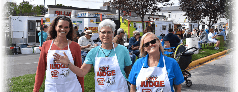 Three smiling food-booth judges in white ‘Best Judge’ aprons at the West Side Nut Club Fall Festival in Evansville