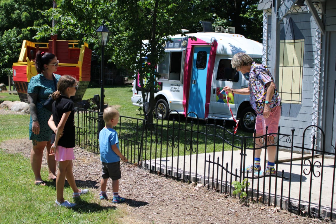 A family watching a costumed entertainer near a red pirate-ship play structure and an ice cream truck at The Fun Farm in Fort Wayne.