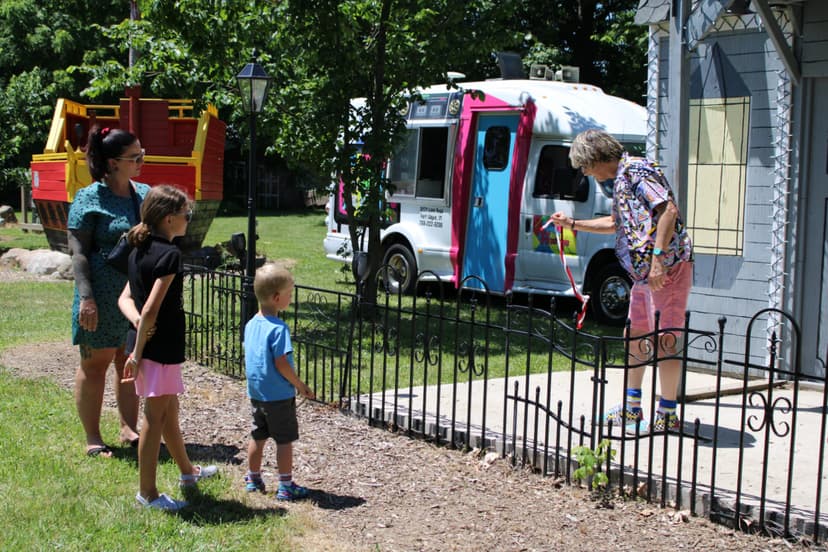 A family watching a costumed entertainer near a red pirate-ship play structure and an ice cream truck at The Fun Farm in Fort Wayne.
