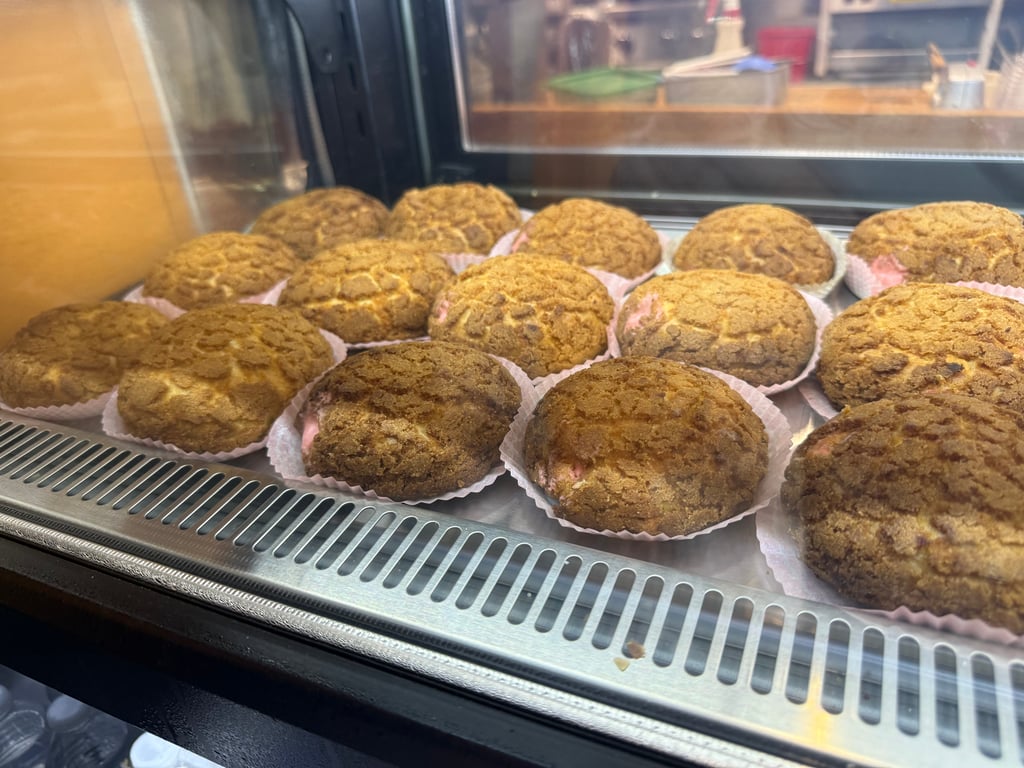 A tray of crackly-topped cream puffs in paper liners inside the René's Bakery case.