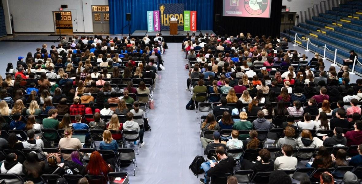 Hundreds of high school students fill an auditorium facing a stage with an IHSPA banner during the Indiana High School Press Association state convention.