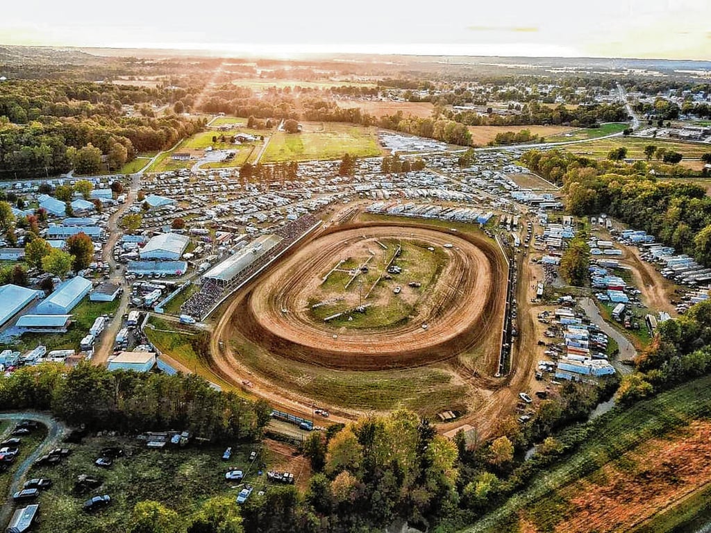 Aerial view at sunset of the dirt oval at Brownstown Speedway ringed by grandstands, race trailers and the packed Jackson County Fairgrounds in Brownstown, Indiana