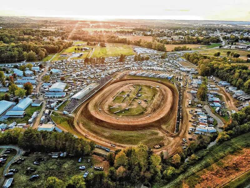 Aerial view at sunset of the dirt oval at Brownstown Speedway ringed by grandstands, race trailers and the packed Jackson County Fairgrounds in Brownstown, Indiana