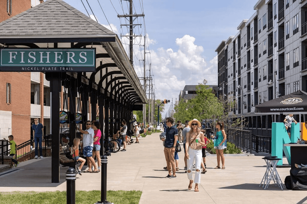 Pedestrians walking the Nickel Plate Trail in downtown Fishers beside a covered walkway and new apartment buildings