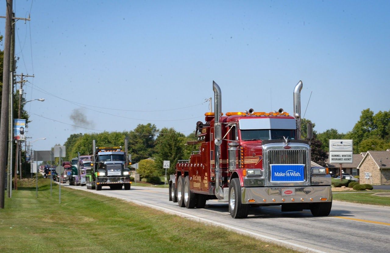 A red Peterbilt tow truck with a Make-A-Wish banner leads a line of big rigs down a rural Indiana highway during the Southern Indiana Truck Convoy.