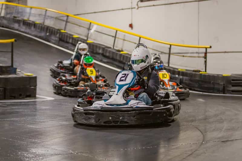 Helmeted drivers racing karts around a turn at Speedway Indoor Karting in Speedway