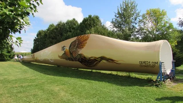 Full-size wind turbine blade painted with a pheasant mural, resting on supports in the grass in Fowler, Indiana