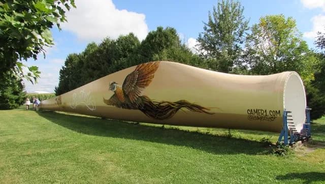 Full-size wind turbine blade painted with a pheasant mural, resting on supports in the grass in Fowler, Indiana