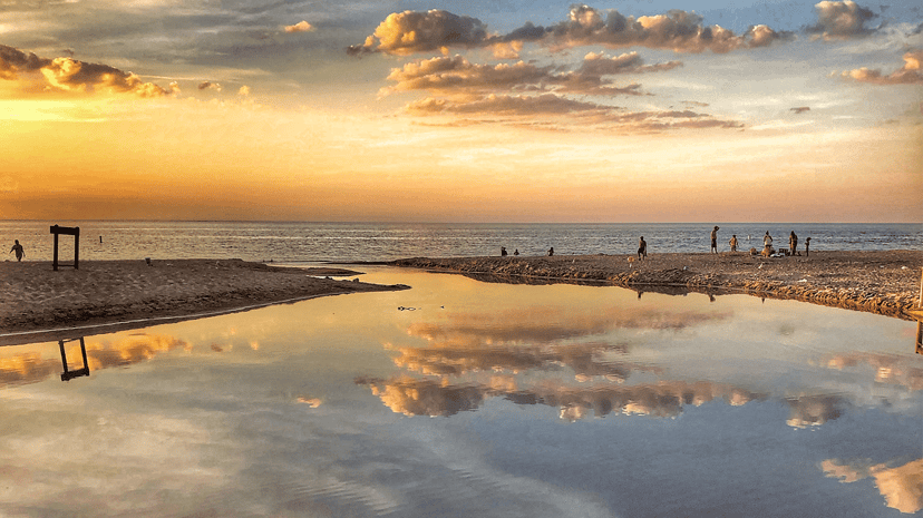 People on a Lake Michigan beach at sunset, with the sky reflected in the calm shallows, in Indiana