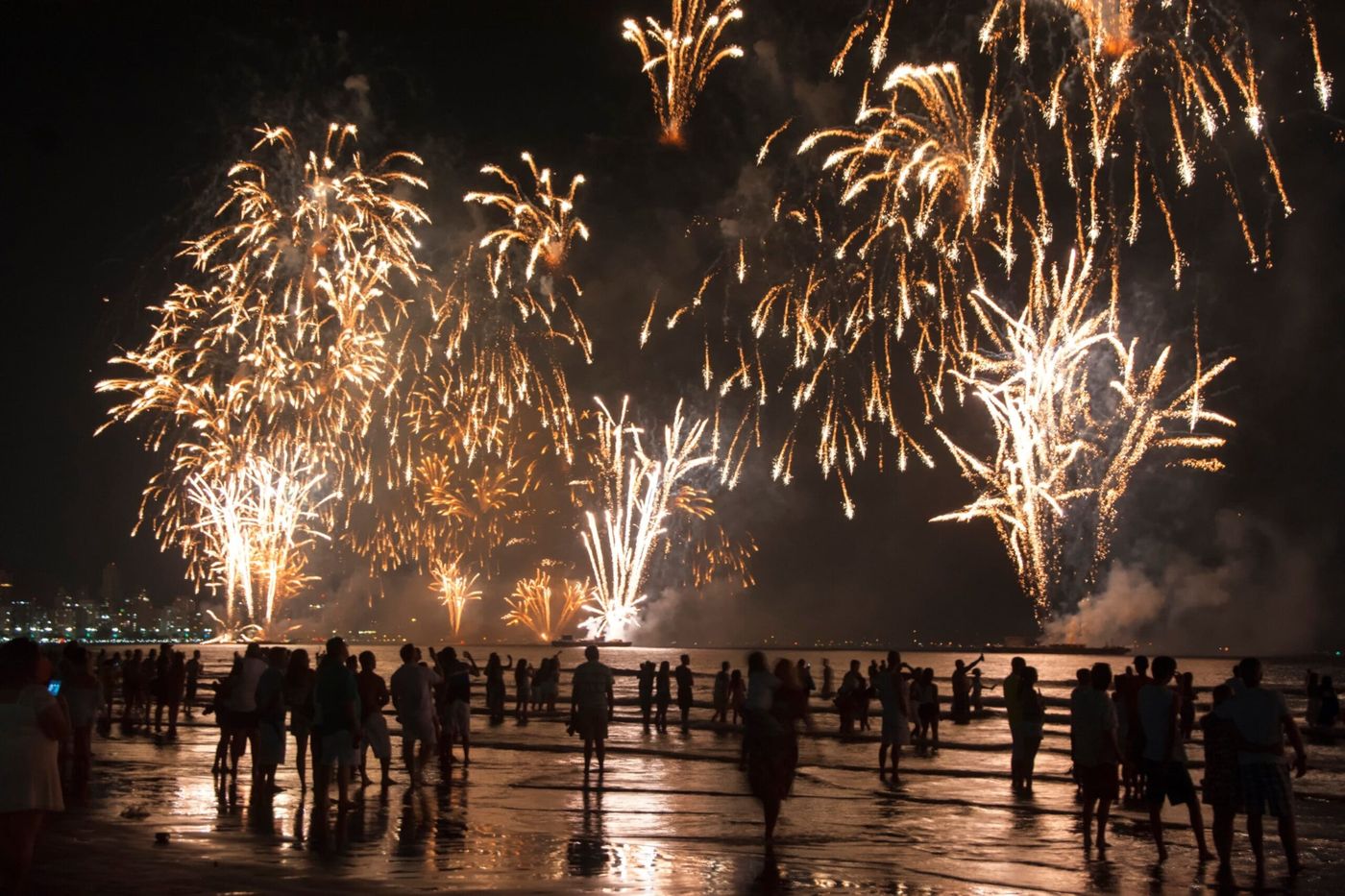 A crowd gathers on the beach to watch a Fourth of July fireworks display burst in golden bursts over the water in Indiana.