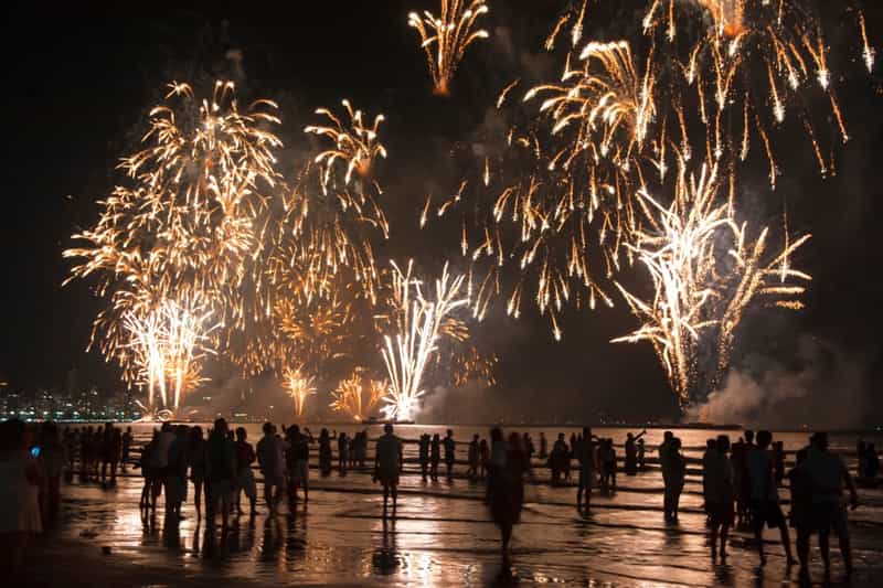 A crowd gathers on the beach to watch a Fourth of July fireworks display burst in golden bursts over the water in Indiana.