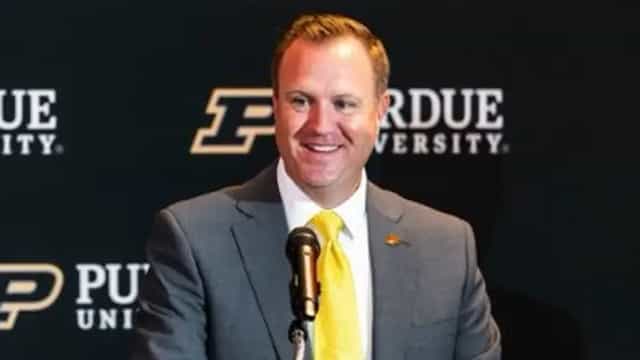Tommy McClelland smiles at a podium during his introduction as Purdue's vice president and director of intercollegiate athletics, in front of a Purdue University backdrop.