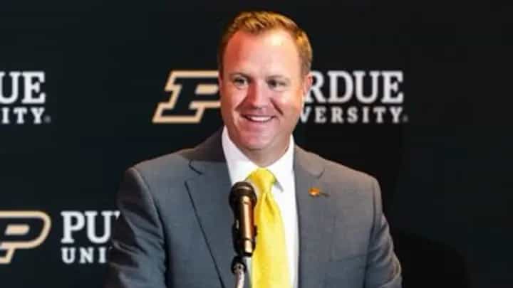 Tommy McClelland smiles at a podium during his introduction as Purdue's vice president and director of intercollegiate athletics, in front of a Purdue University backdrop.