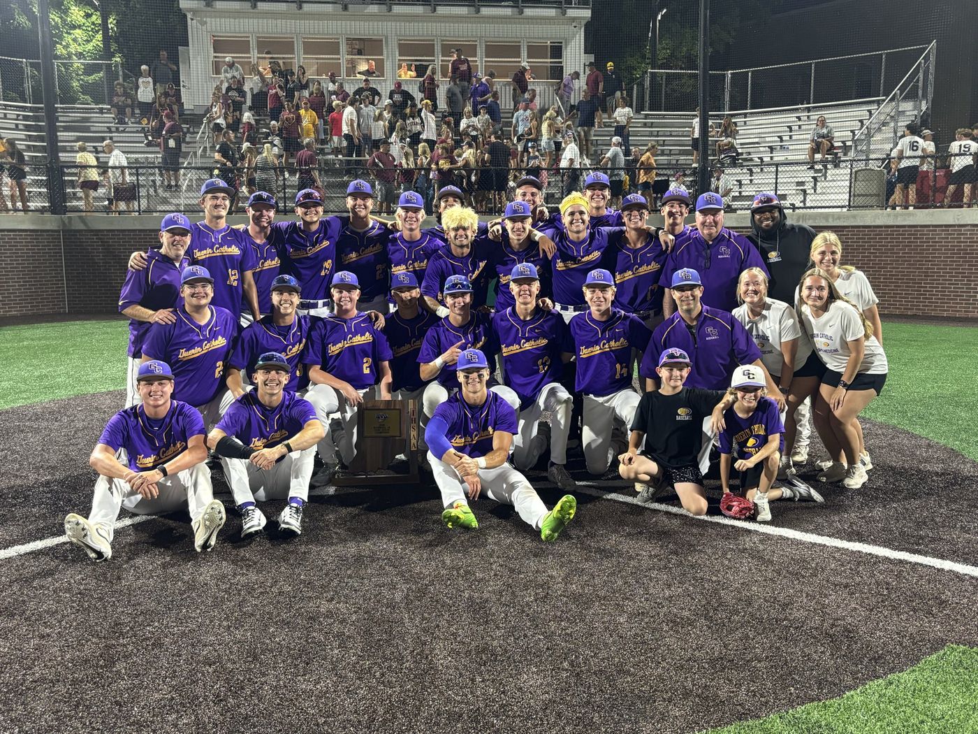 The Guerin Catholic Golden Eagles baseball team poses with their semi-state championship trophy on the infield at night ahead of the 2026 IHSAA Class 3A state finals.