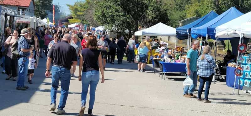 Crowds walking a street lined with vendor tents and craft booths in Metamora on a sunny fall day