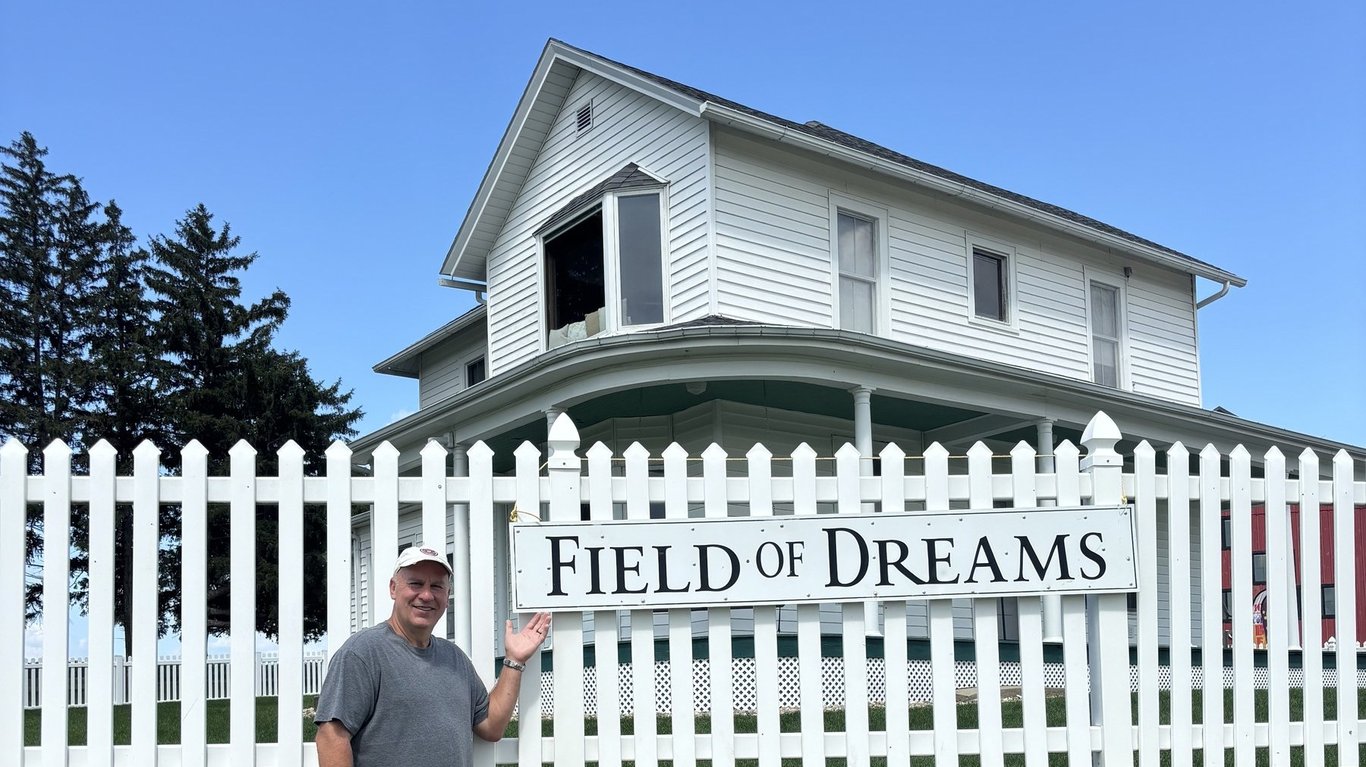 A visitor stands beside the white Field of Dreams sign on the picket fence in front of the movie-site farmhouse in Dyersville, Iowa.