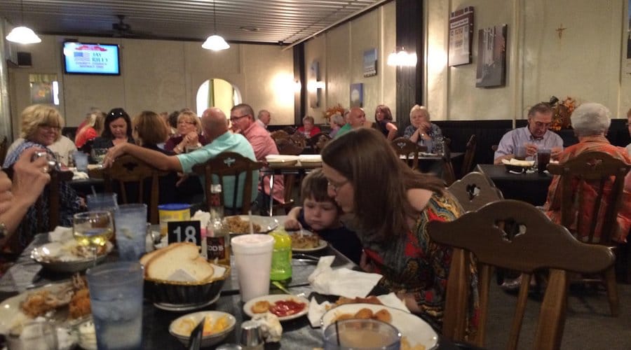 A packed dining room at the Carriage Inn in Haubstadt, Indiana, with families gathered around tables set with fresh bread, drinks and homestyle comfort food.