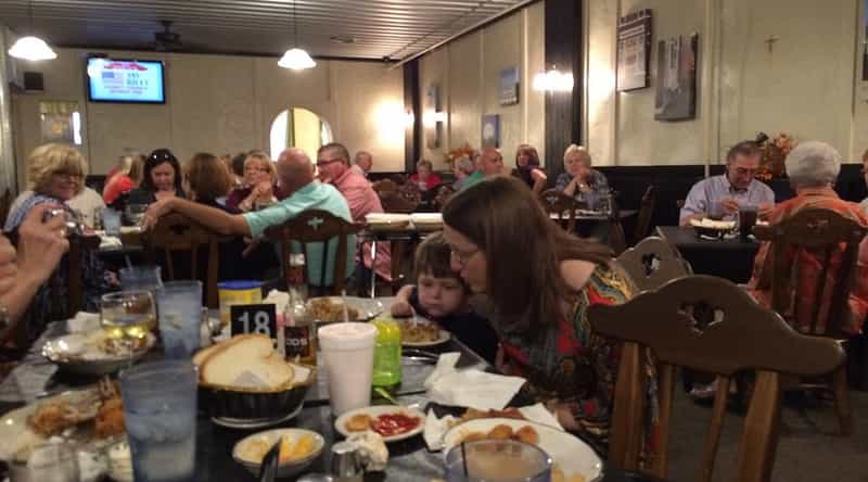 A packed dining room at the Carriage Inn in Haubstadt, Indiana, with families gathered around tables set with fresh bread, drinks and homestyle comfort food.