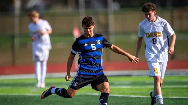Castle boys soccer player in a blue and black No. 5 jersey strikes the ball as a Carmel player in white follows during the semi-state match