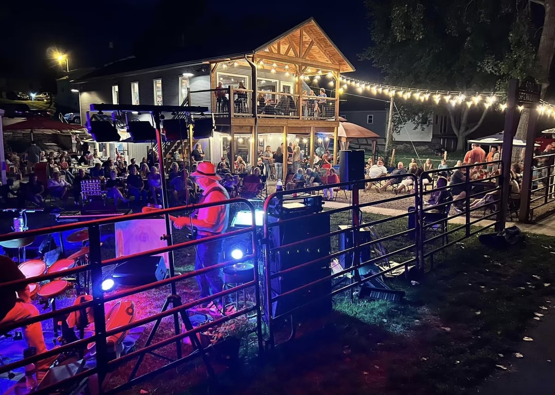 Nighttime crowd gathered on the lawn at 950 Speakeasy Bistro in Lagro, Indiana, watching a live band play under string lights beside the two-story timber patio