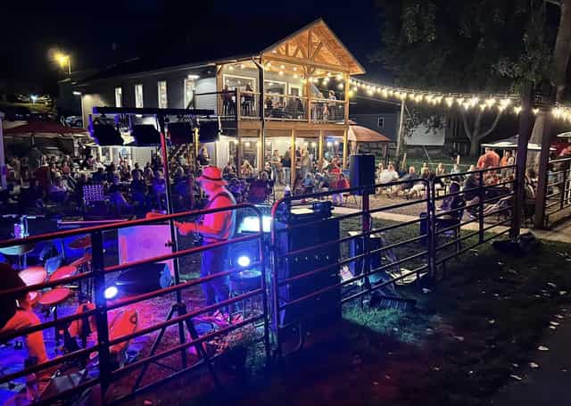 Nighttime crowd gathered on the lawn at 950 Speakeasy Bistro in Lagro, Indiana, watching a live band play under string lights beside the two-story timber patio