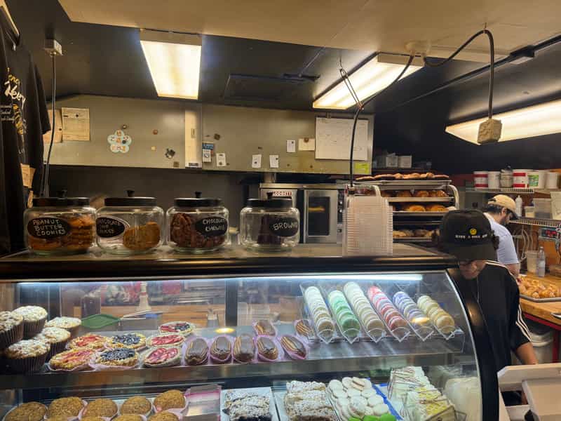 The counter at René's Bakery in Broad Ripple, with glass jars of peanut butter, chocolate chip and chocolate chewy cookies above a case of pastries as bakers work behind it.
