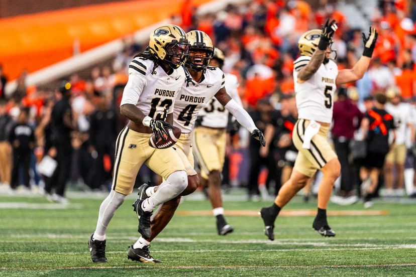 Purdue defenders in gold pants celebrate as No. 13 carries the football in front of orange-clad Illinois fans at Gies Memorial Stadium in Champaign