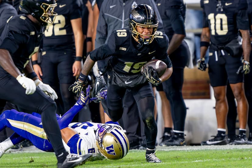 Purdue ball carrier No. 19 in a black uniform runs past a diving Washington defender along the sideline at Ross-Ade Stadium