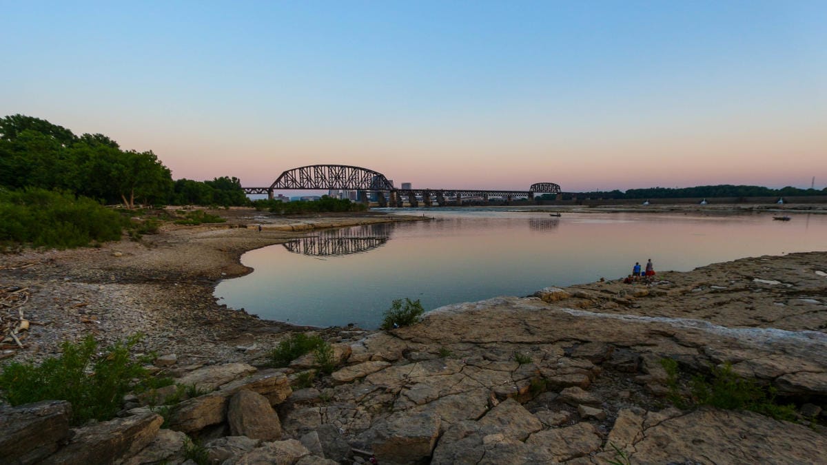 Sunset over the exposed limestone fossil beds and a still river pool at Falls of the Ohio State Park in Clarksville, Indiana, with a steel truss bridge crossing the Ohio River
