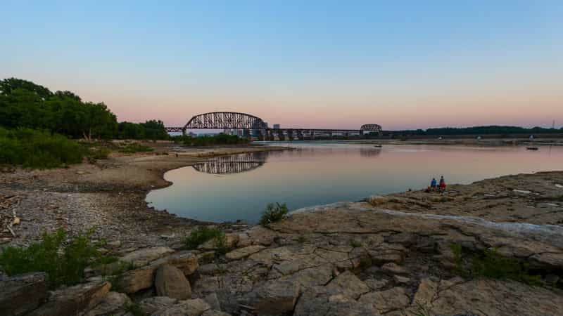Sunset over the exposed limestone fossil beds and a still river pool at Falls of the Ohio State Park in Clarksville, Indiana, with a steel truss bridge crossing the Ohio River