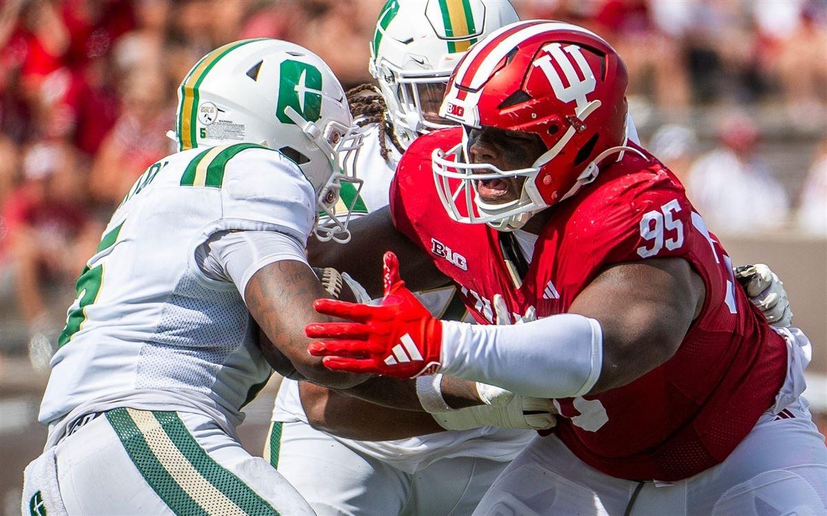 Indiana defensive tackle No. 95 fights through a block from an opposing lineman in green and gold at the line of scrimmage