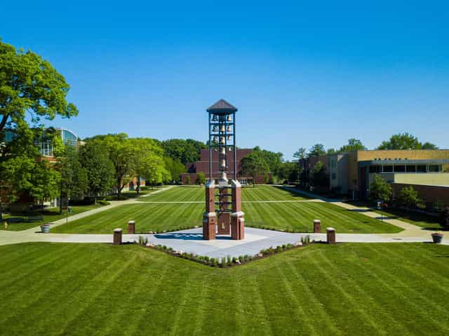 The bell tower on the Manchester University mall, surrounded by striped green lawns and campus buildings under a clear blue sky in North Manchester, Indiana