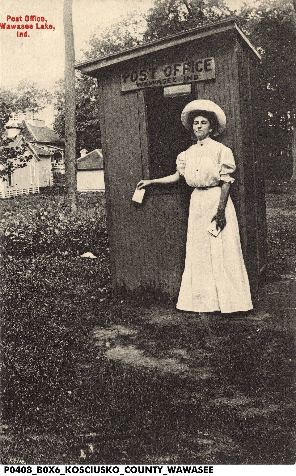 Vintage postcard of a woman in a white dress and wide hat mailing a letter at the tiny wooden Wawasee, Ind. post office