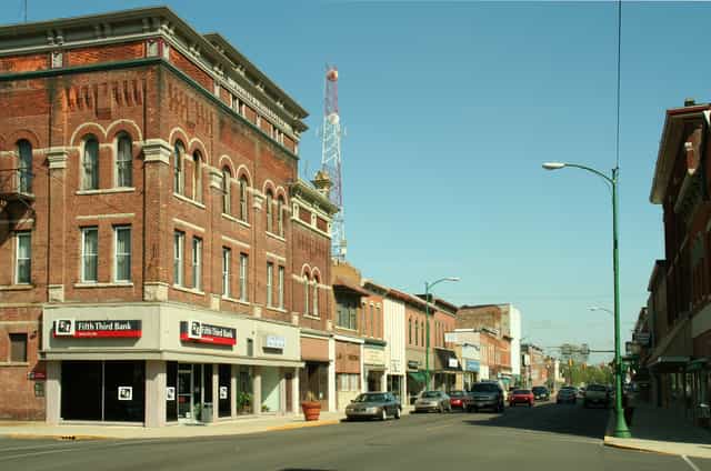 Historic brick storefronts along a downtown street in Decatur, Indiana, with a three-story corner building and US 224 route signs at the intersection ahead