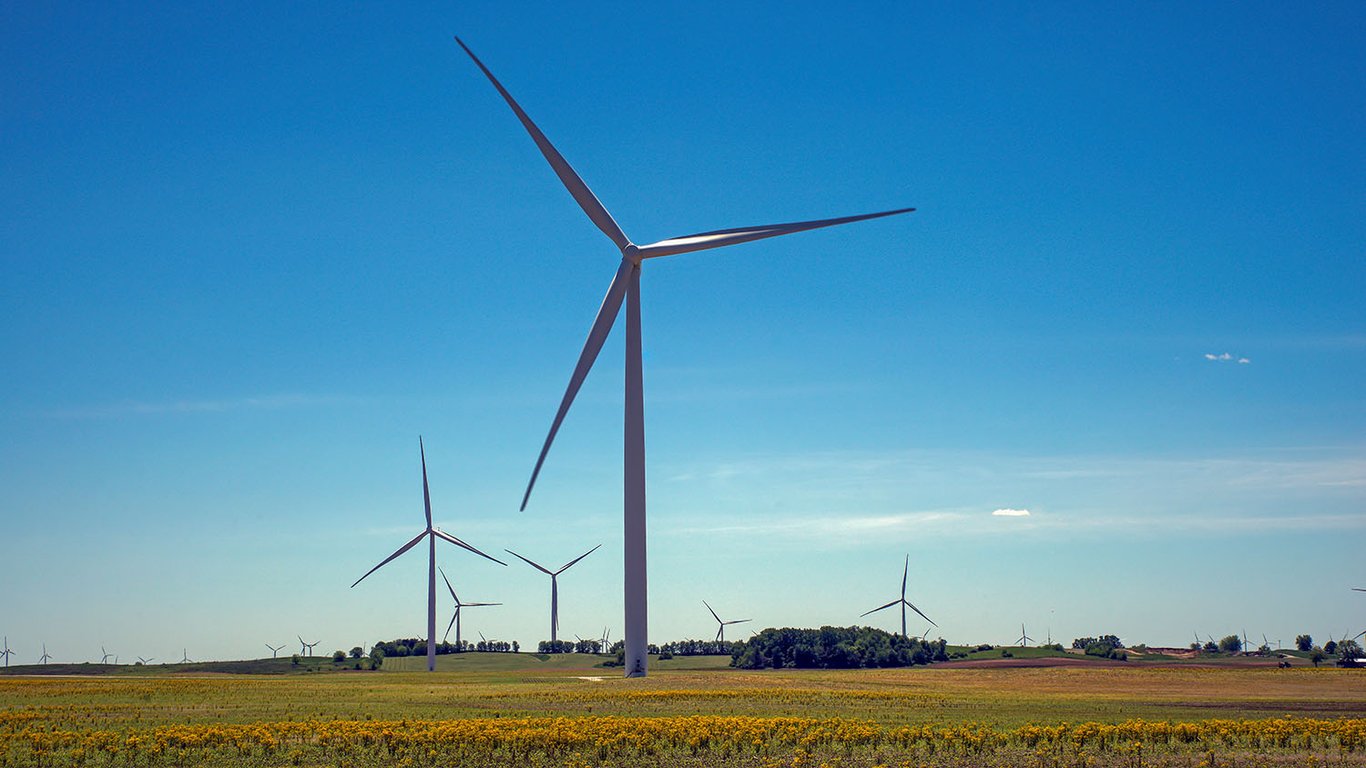 Wind turbines standing over a flat field of yellow wildflowers under a clear blue sky in Benton County wind country