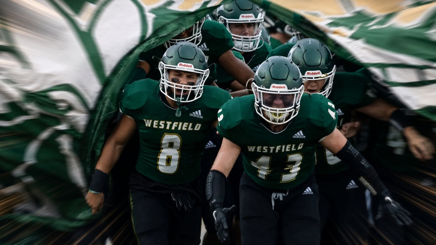 Westfield Shamrocks football players in green jerseys and helmets run through a green and white banner onto the field before a game