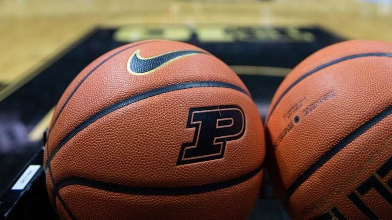 Two Nike basketballs stamped with the Purdue Boilermakers P logo sitting courtside on a gold and black hardwood floor