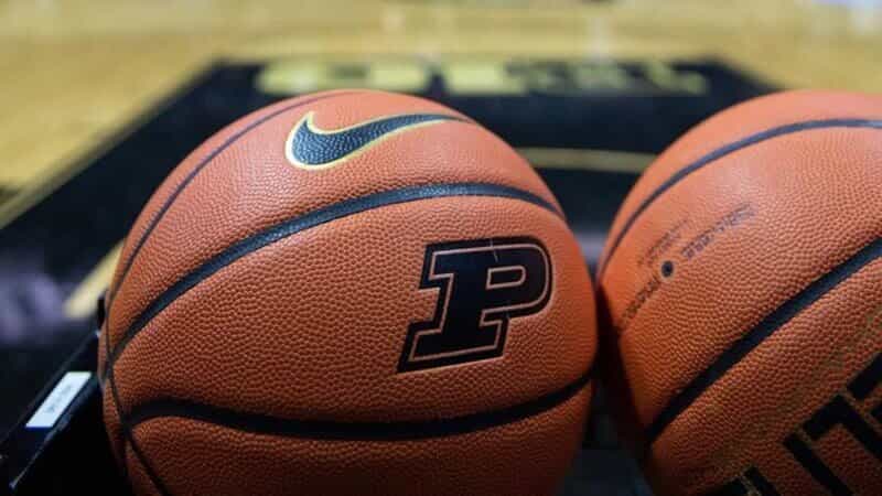 Two Nike basketballs stamped with the Purdue Boilermakers P logo sitting courtside on a gold and black hardwood floor