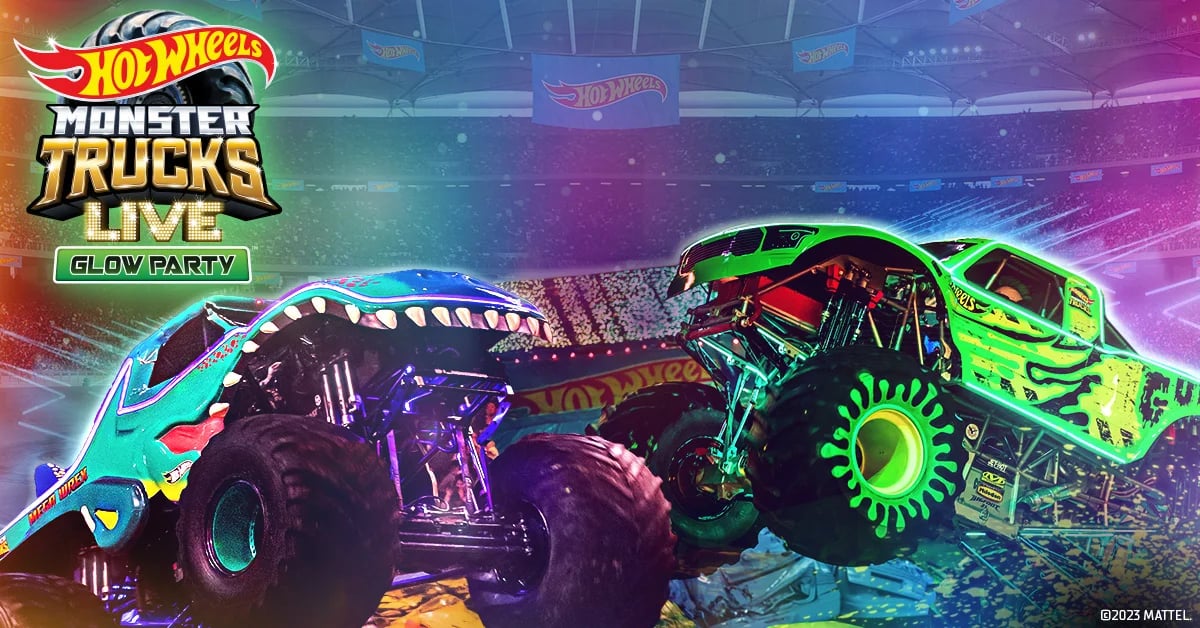 Two Hot Wheels Monster Trucks lit up in bright neon colors mid-show at a Hot Wheels Monster Trucks Live arena event