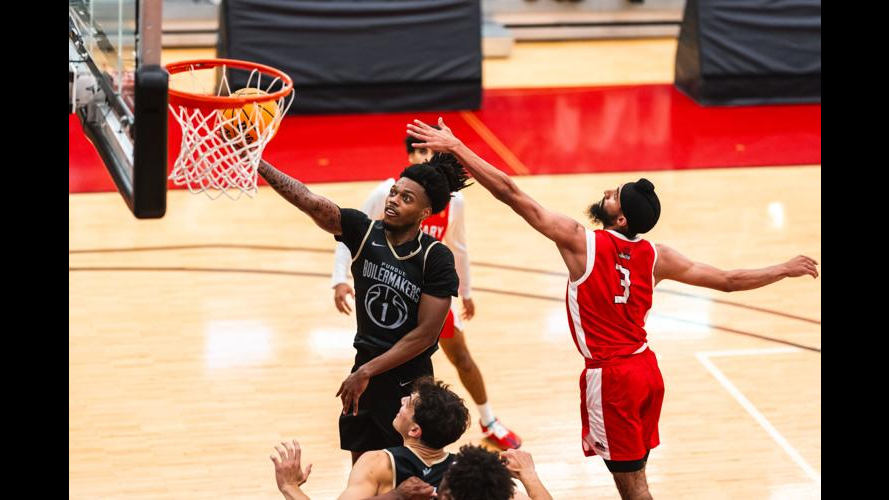 A Purdue Boilermakers player in a black jersey rises for a layup at the rim as a defender in a red jersey contests the shot during an exhibition game in Canada