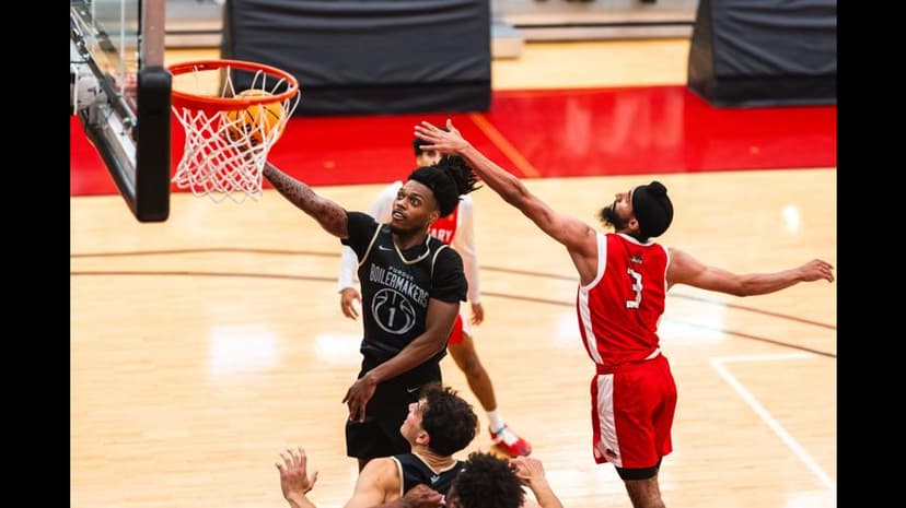 A Purdue Boilermakers player in a black jersey rises for a layup at the rim as a defender in a red jersey contests the shot during an exhibition game in Canada