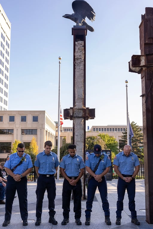 Five Indianapolis firefighters stand with heads bowed beneath the bronze eagle on a World Trade Center beam at the Indiana 9/11 Memorial.