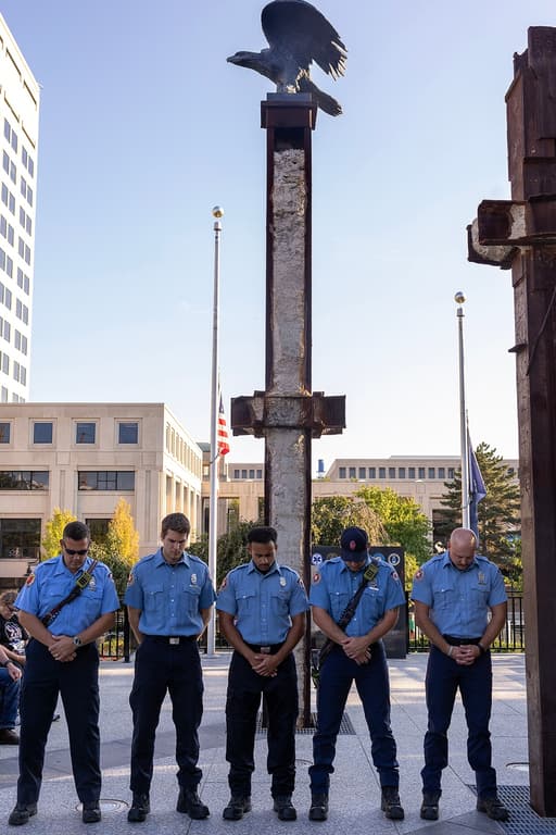 Five Indianapolis firefighters stand with heads bowed beneath the bronze eagle on a World Trade Center beam at the Indiana 9/11 Memorial.