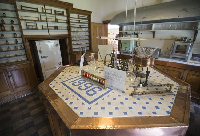 A hexagonal laboratory table tiled with the date 1896, set with glassware and test tubes inside an original wood-paneled lab at the Indiana Medical History Museum.