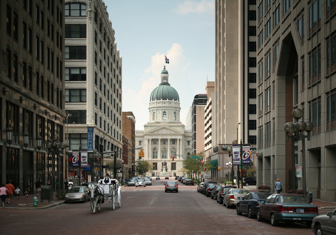 The Indiana Statehouse dome at the end of Market Street in downtown Indianapolis, with a horse-drawn carriage on the brick street