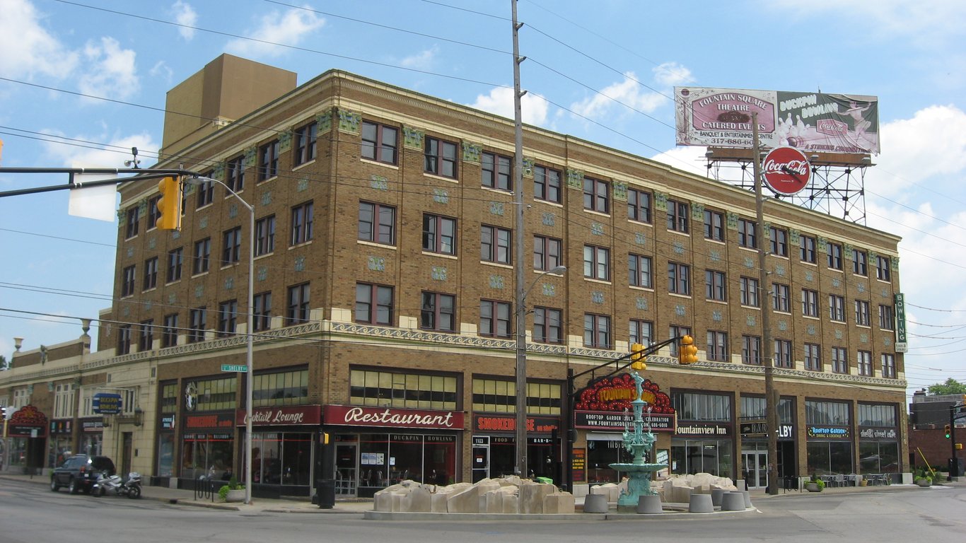 Corner view of the brick Fountain Square Theatre building on Shelby Street in Indianapolis, with ground-floor restaurant signs, a small fountain and a street intersection in the foreground