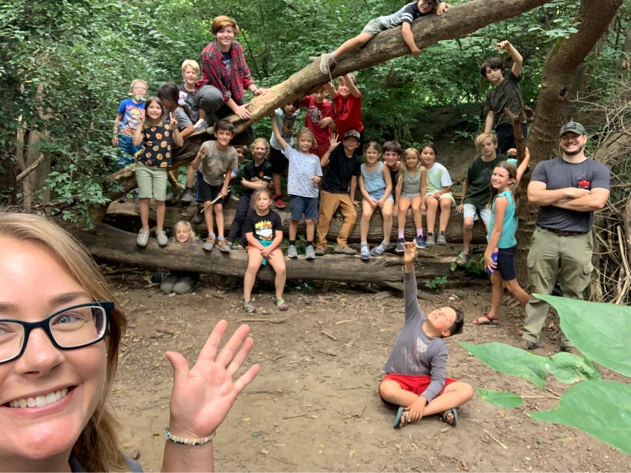 Children and instructors gather on a fallen log in the woods during a White Pine Wilderness Academy forest school session in Indianapolis.