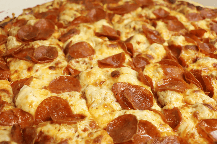 A close-up of a cracker-thin, square-cut pepperoni Una pizza with cheese spread to the edge