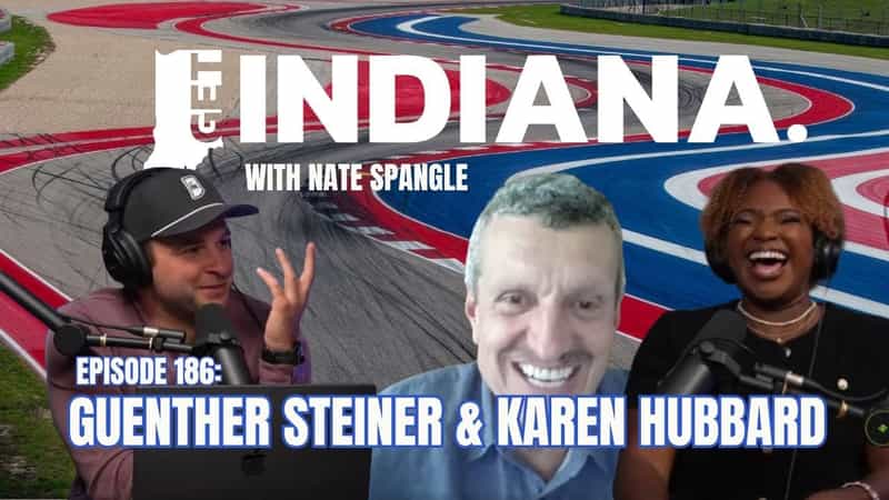 Podcast hosts discuss bobsledding aspirations against a vibrant racetrack backdrop in Indiana.